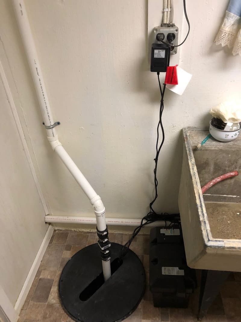 Installed sump pump with white discharge pipe in basement corner