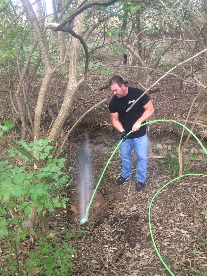 Worker using a green hose to flush a wooded area