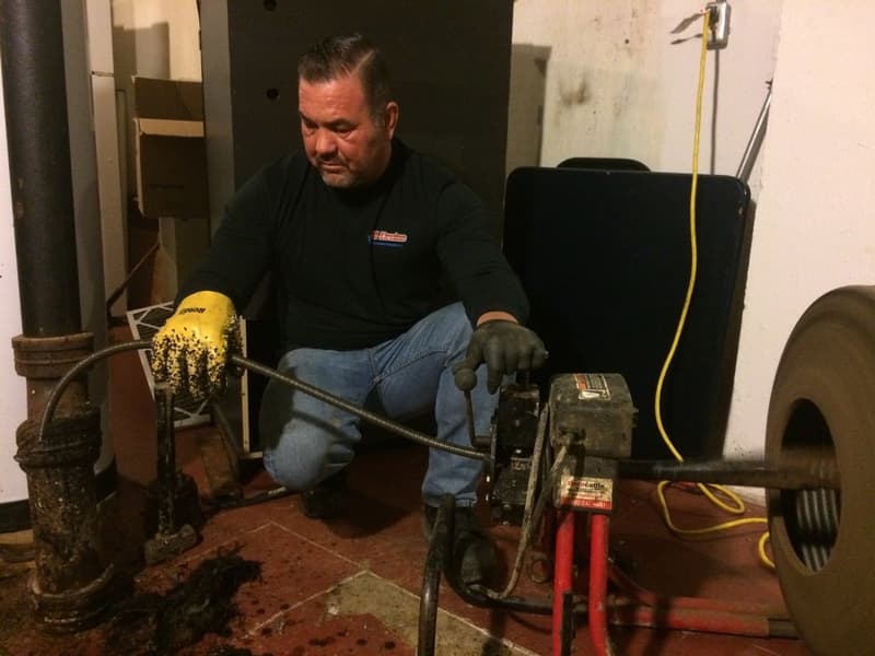 Technician operating a drain cleaning machine in a basement