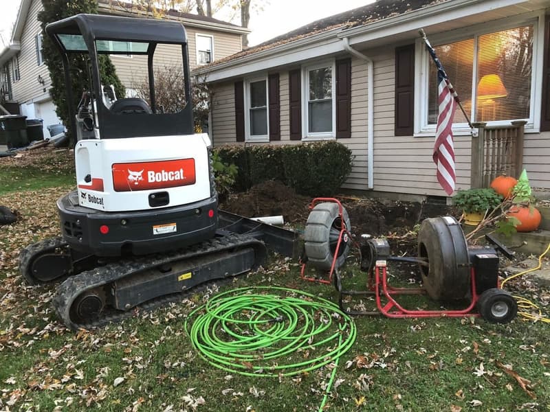Mini excavator and drain cleaning machines on a home lawn